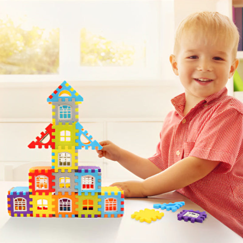 Enfant de 3-4 ans concentré construisant une tour architecturale complexe BuildCréa sur table. Blocs bleu, rouge, jaune et violet assemblés avec précision. Développement de la patience, de la coordination et des compétences de résolution de problèmes dans un cadre ludique.