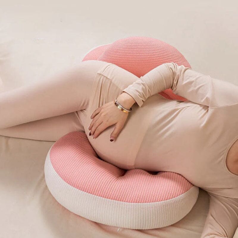 Femme enceinte assise confortablement avec coussin de grossesse rose offrant soutien lombaire optimal pour position assise prolongée