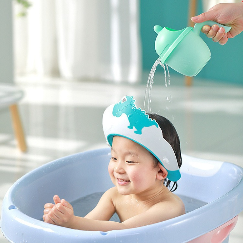 Enfant protégé par bonnet de bain dinosaure vert pendant rinçage, eau versée sans contact avec les yeux