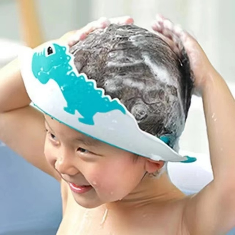 Enfant souriant pendant le lavage des cheveux avec bonnet de bain dinosaure bleu, protection totale contre l'eau et le shampoing