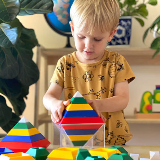 Garçon blond concentré construisant pyramide avec blocs de construction colorés - jeu éducatif enfant