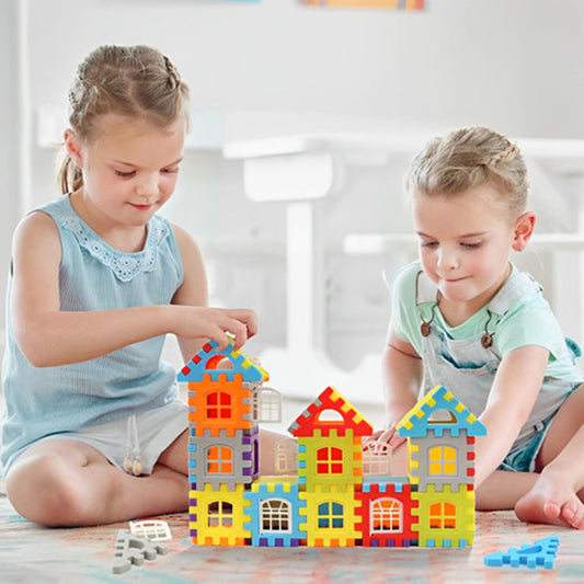 Deux enfants de 3-5 ans assis au sol créant ensemble un village coloré BuildCréa. Rangée de maisons avec toits et fenêtres en rouge, bleu, jaune et violet. Coopération, partage et imagination collective dans un environnement d'apprentissage social.