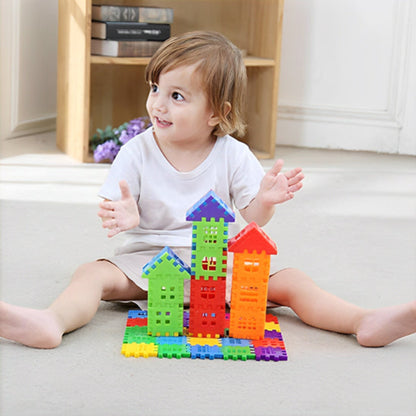 Enfant de 2-3 ans assis au sol créant avec fierté ses premières tours BuildCréa. Structure colorée de trois maisons aux toits triangulaires rouge, jaune, vert et bleu sur tapis moelleux. Développement de la motricité fine et de la créativité dans un environnement familial chaleureux.