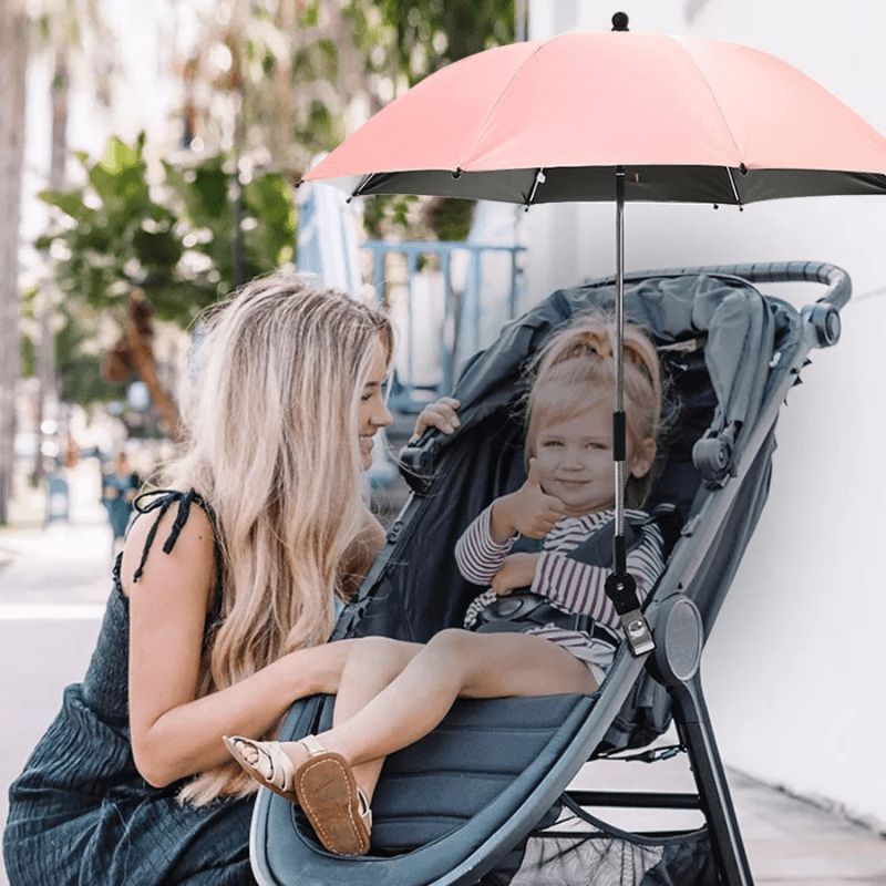 Maman avec enfant en poussette protégé par parapluie pare-soleil rose lors d'une promenade ensoleillée en extérieur